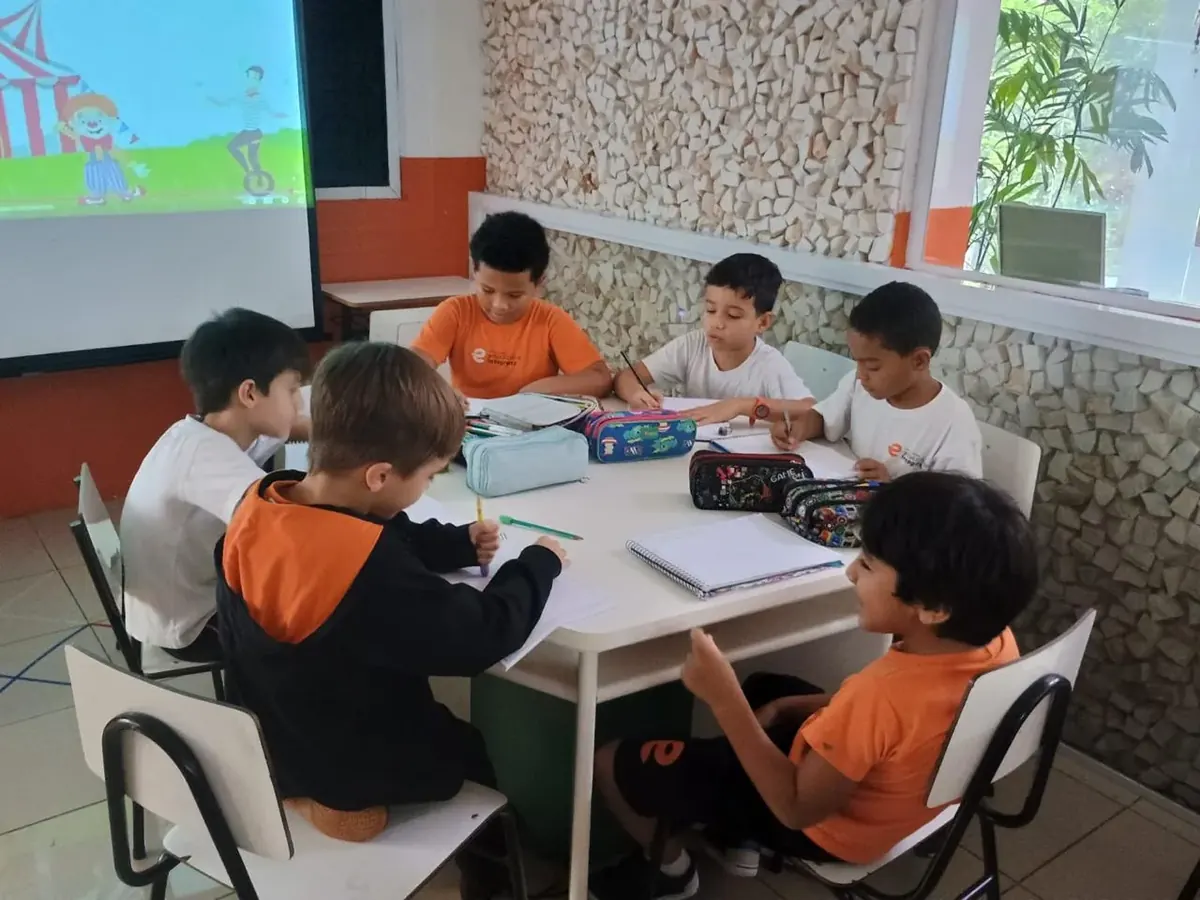 Turma trabalhando em grupo nas mesas, com a aula projetada na parede