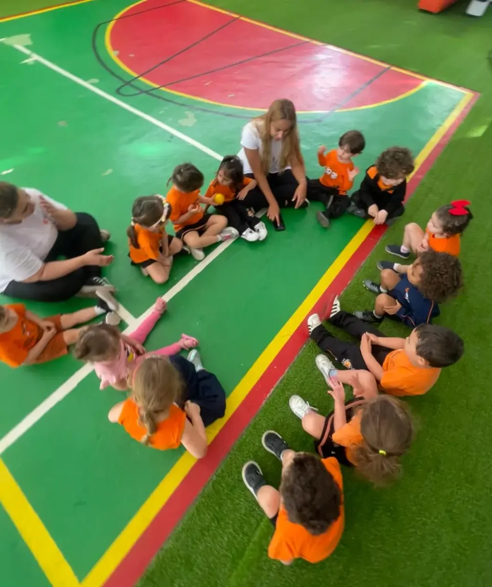 Turma da Educação Infantil em roda com as professoras, na quadra