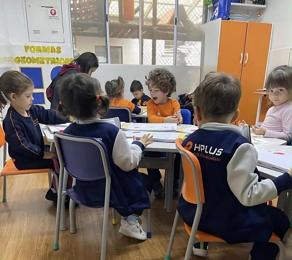 Turma da Educação Infantil em atividade de formas geométricas, sentada em volta das mesas com a professora