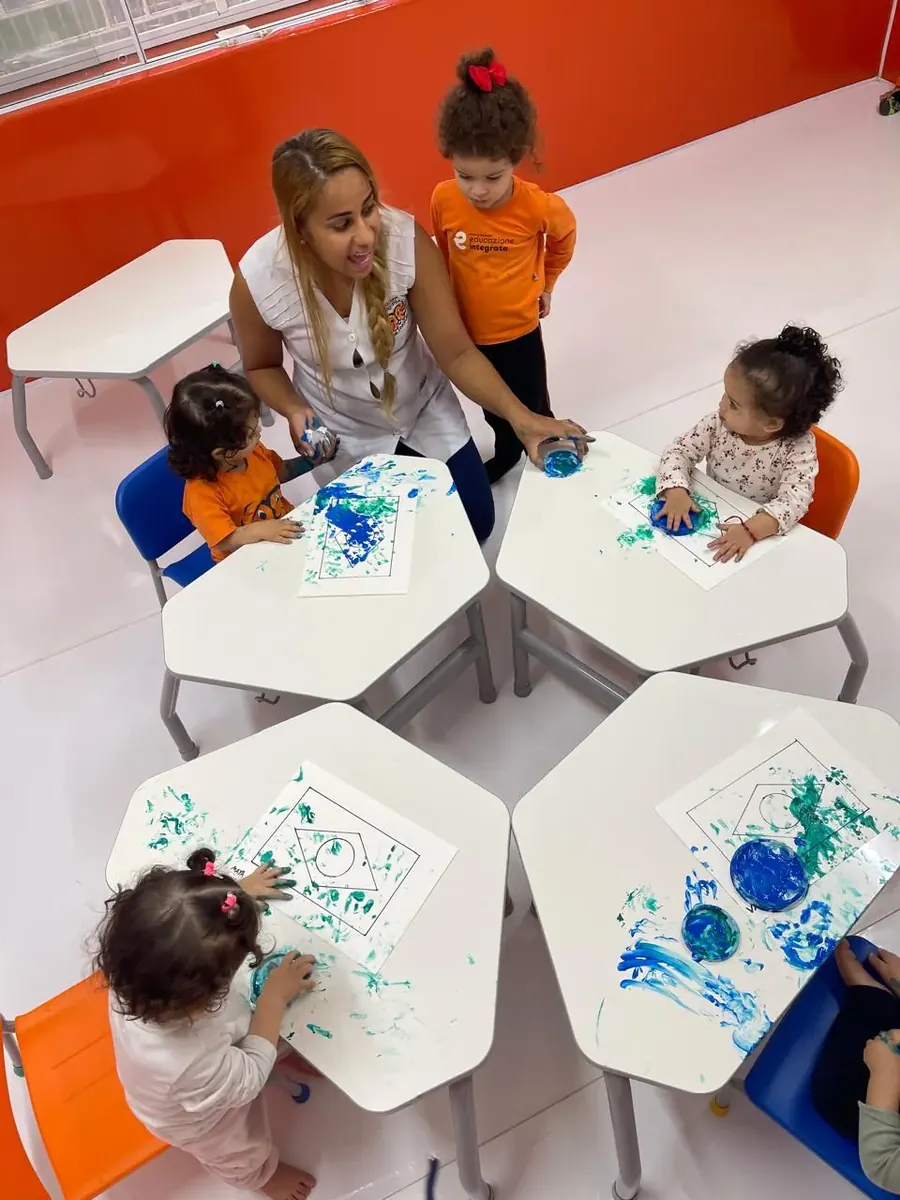 Turma do Mini Maternal pintando com as mãos nas mesas, acompanhada pela professora